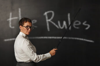 College instructor standing in front of a blackboard that says, "The Rules"